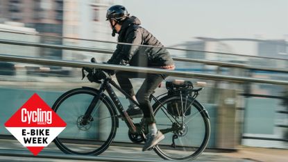 Ribble electric bike is ridden by a rider wearing all black clothing with a blurred background. 