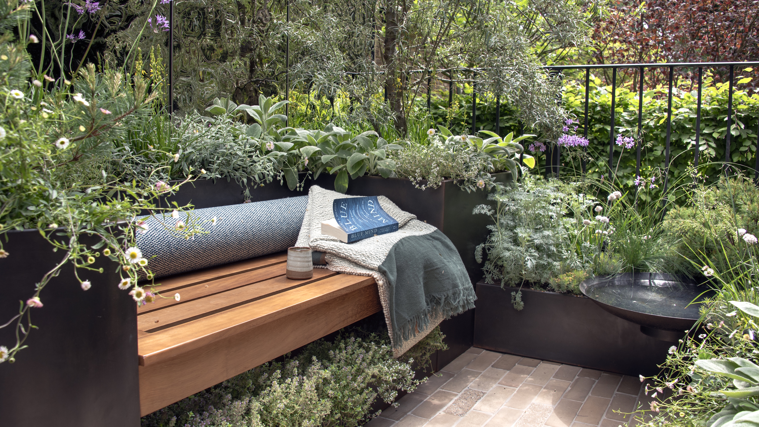 A wooden bench in a small balcony garden surrounded by raised planters at the Chelsea Flower Show