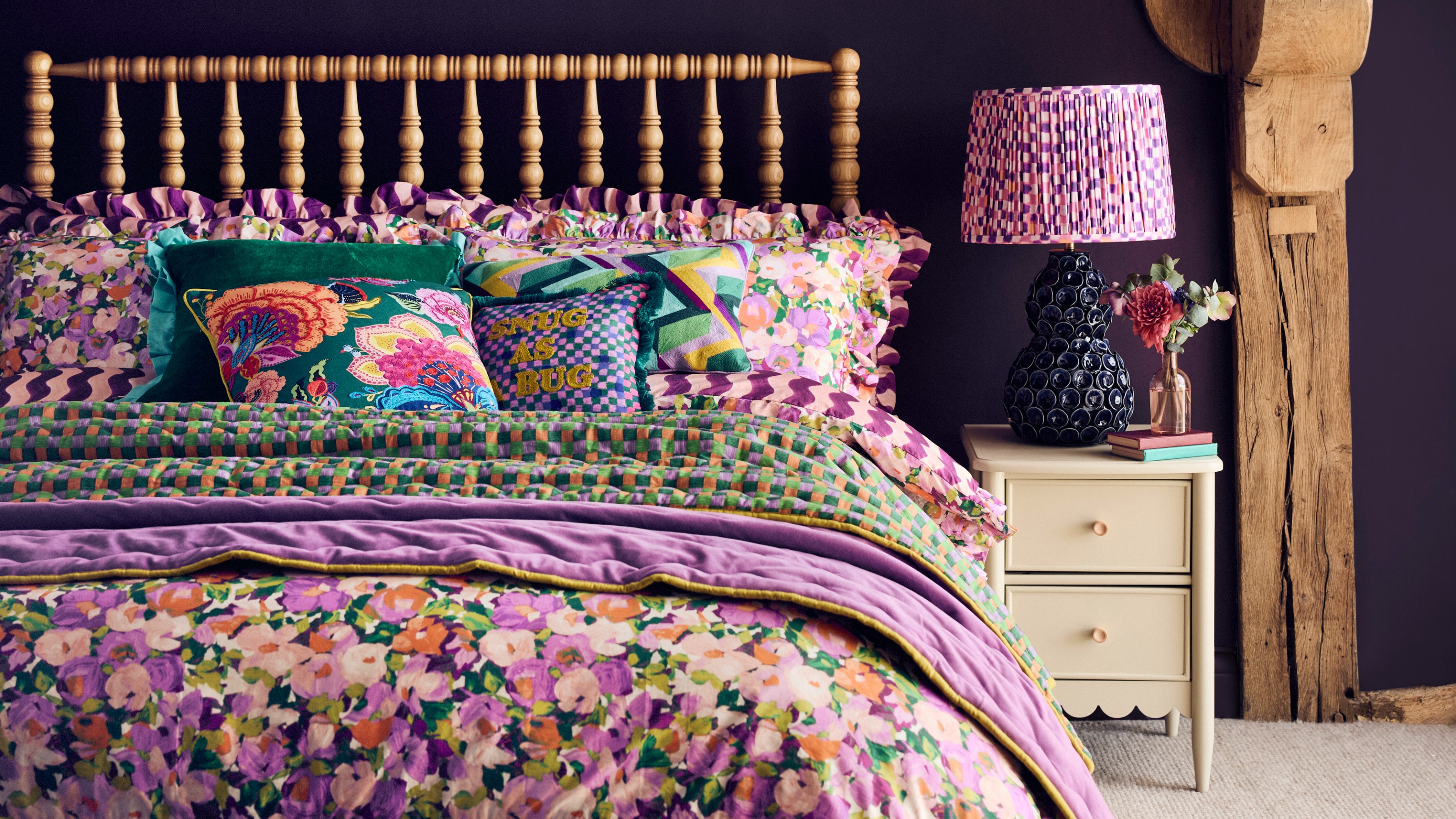A bedroom with a bobbin bed frame covered with floral bed linen and a ceramic table lamp from the Dunelm x Sophie Robinson collection on the bedside table