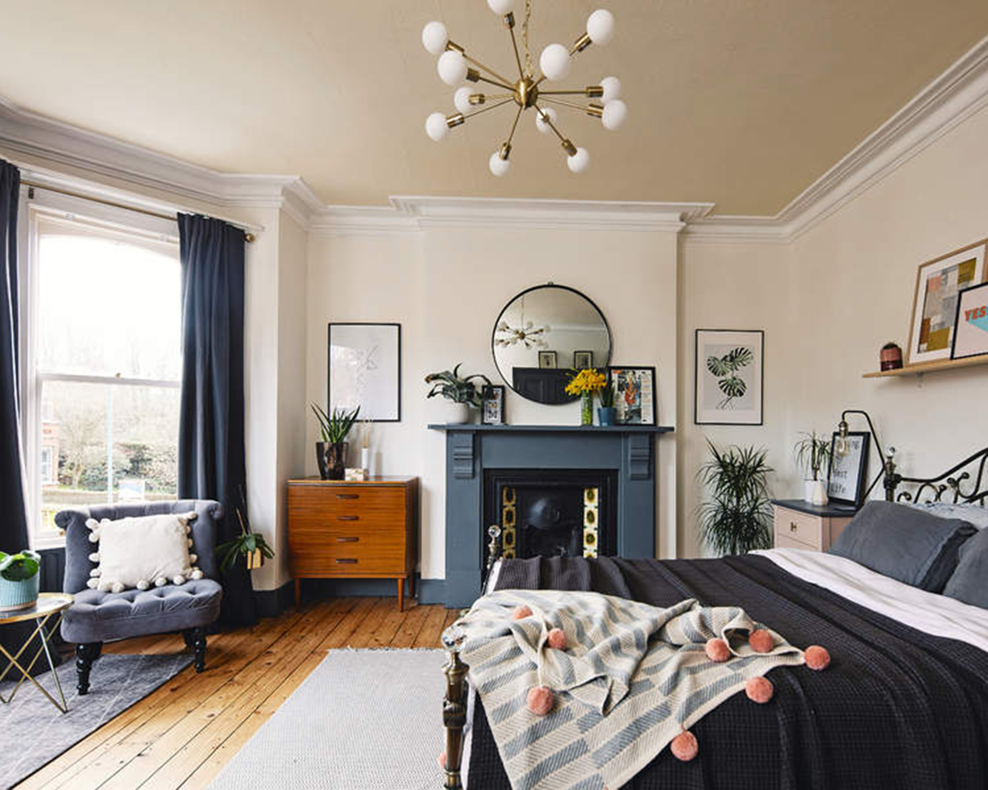 A navy and white bedroom with fireplace, bed, navy curtain window treatment, wooden flooring, shelves above bed and round glass coffee table decor