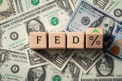 Wooden blocks spelling FED% with a green arrow on a background of cash.