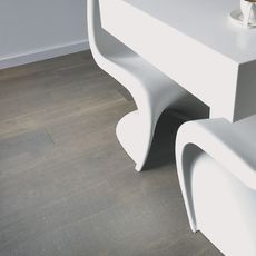 A close up view of pale wooden flooring in a room with a white table, modern white plastic chairs, and white walls.