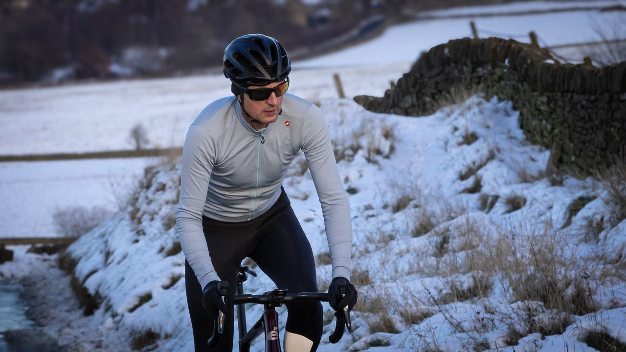 Male cyclist riding up a snowy lane wearing one of the best long sleeved cycling jerseys 