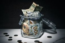A jar full of various US dollar bills surrounded by coins