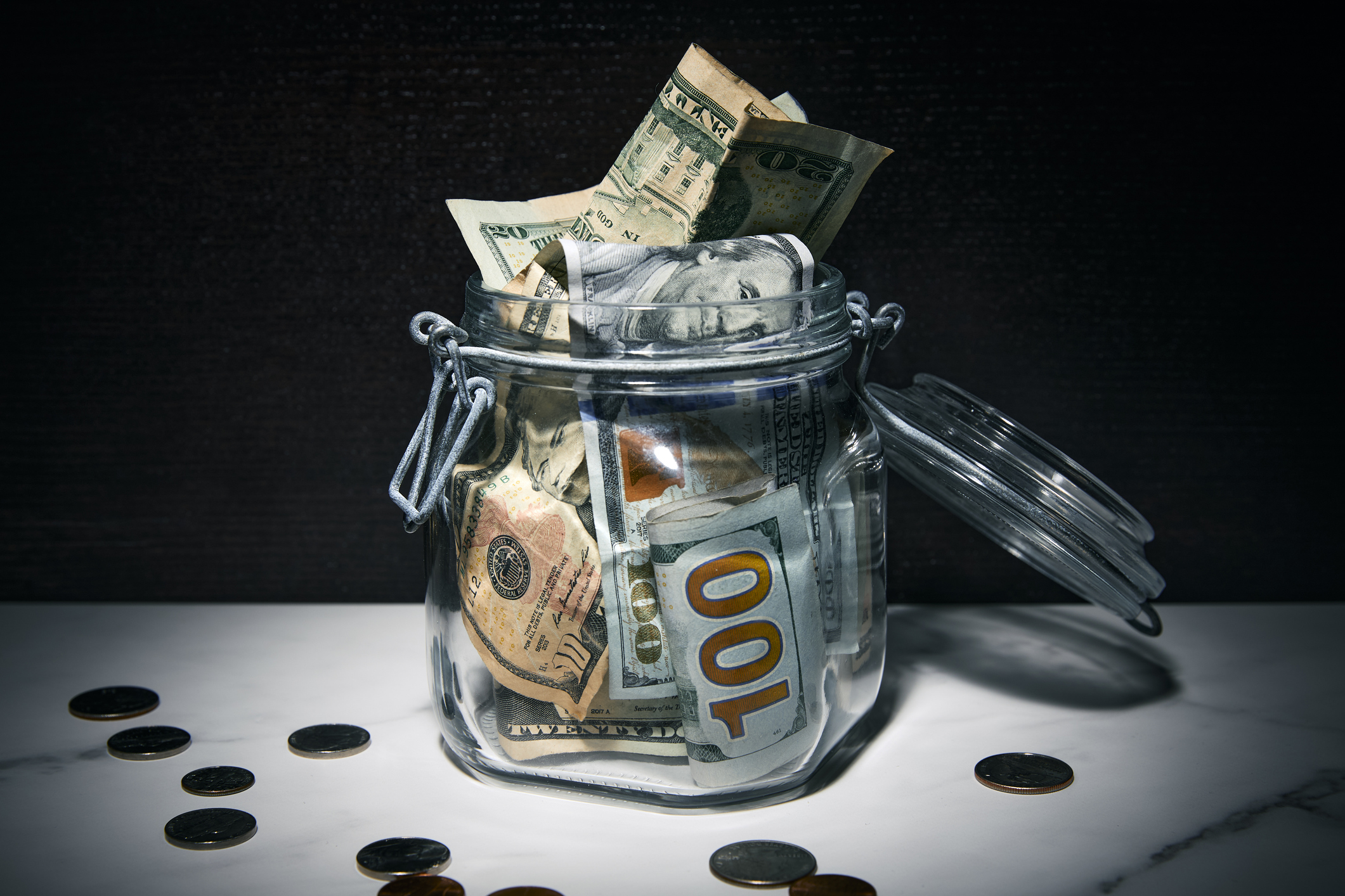 A jar full of various US dollar bills surrounded by coins