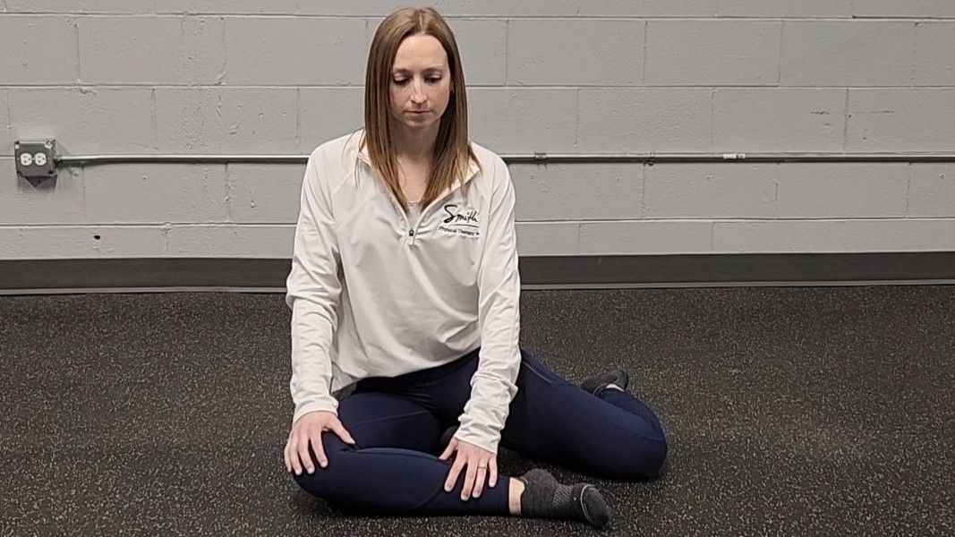 Woman demonstrating stretch. She wears a white long-sleeve top, blue sports leggings and black socks