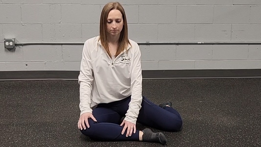Woman demonstrating stretch. She wears a white long-sleeve top, blue sports leggings and black socks