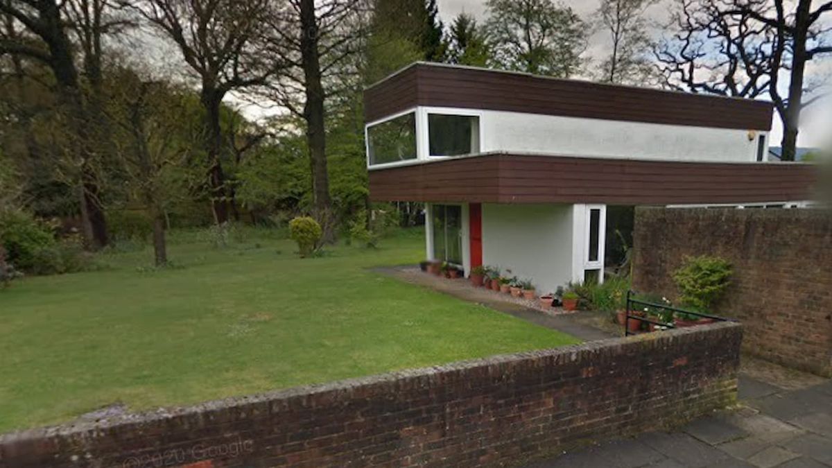 A front on shot of a two storey listed building with a brick front wall and its garden 