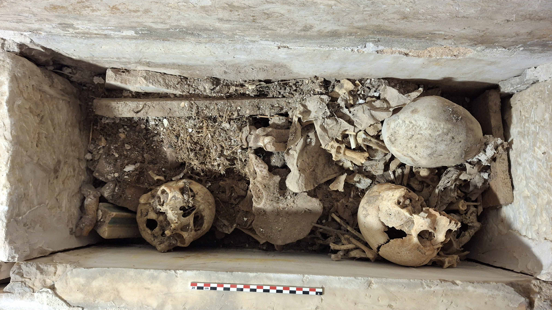 a pile of human bones including at least three large skulls in a carved stone niche
