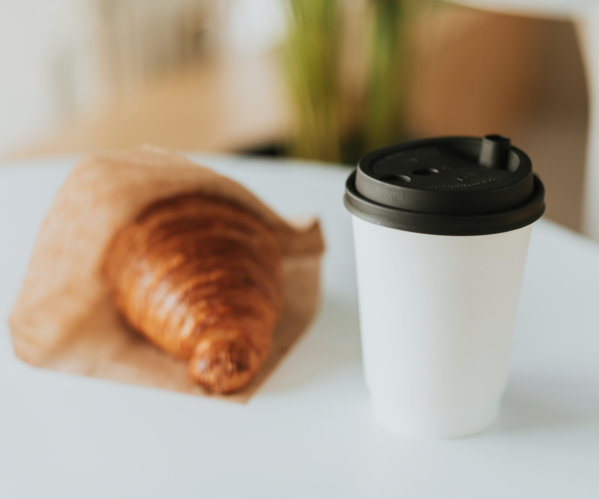 takeaway coffee cup and croissant in paper packaging on white table
