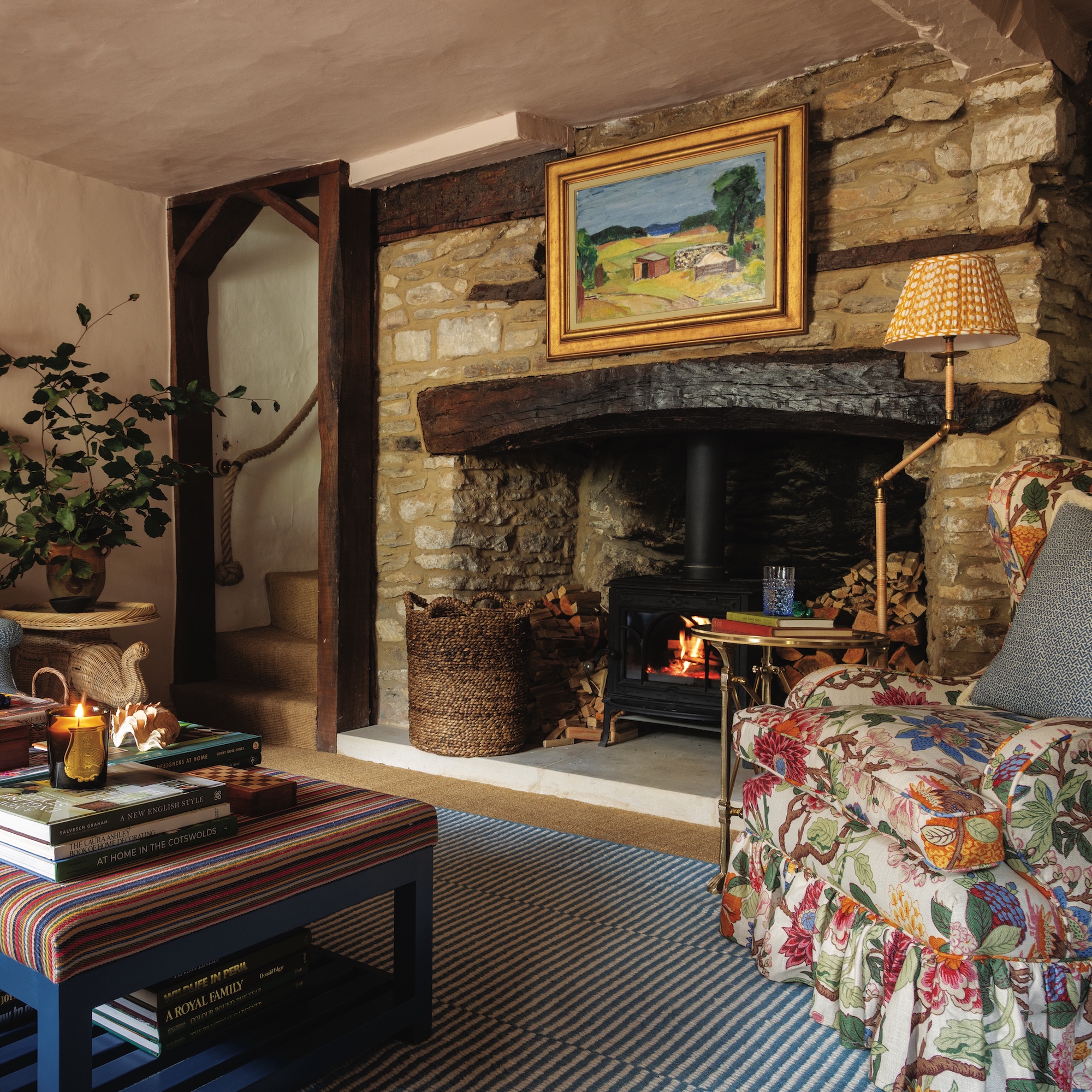 sitting room in a cottage with stone walls and large fireplace with upholstered armchair and striped ottoman
