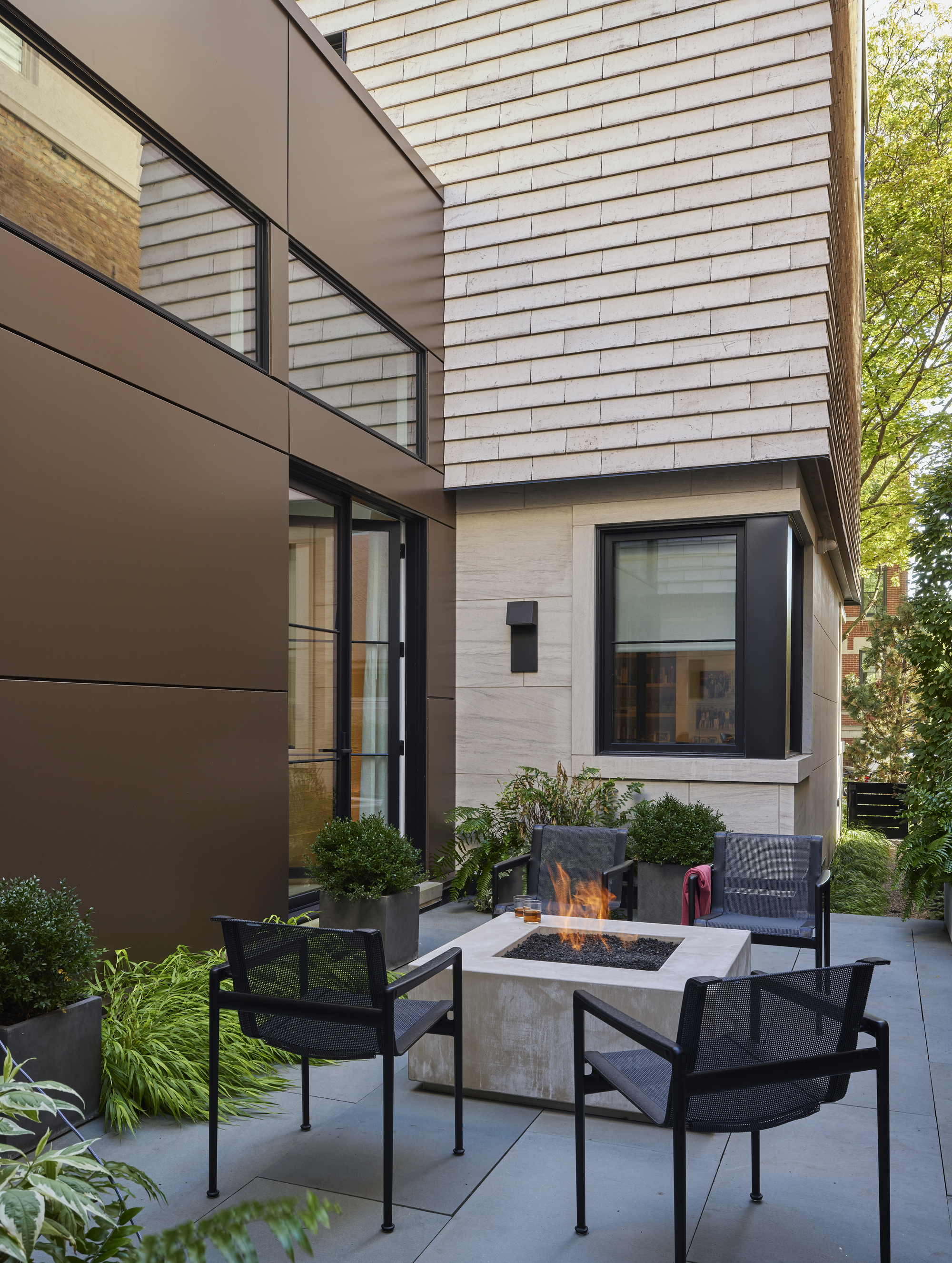 outdoor area with four armchairs around a firepit, one paved courtyard with planter boxes, and the exterior of the house
