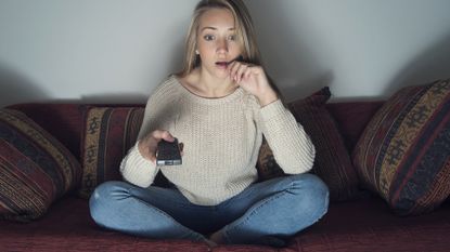 Young woman shocked watching a film and pointing remote at the tv