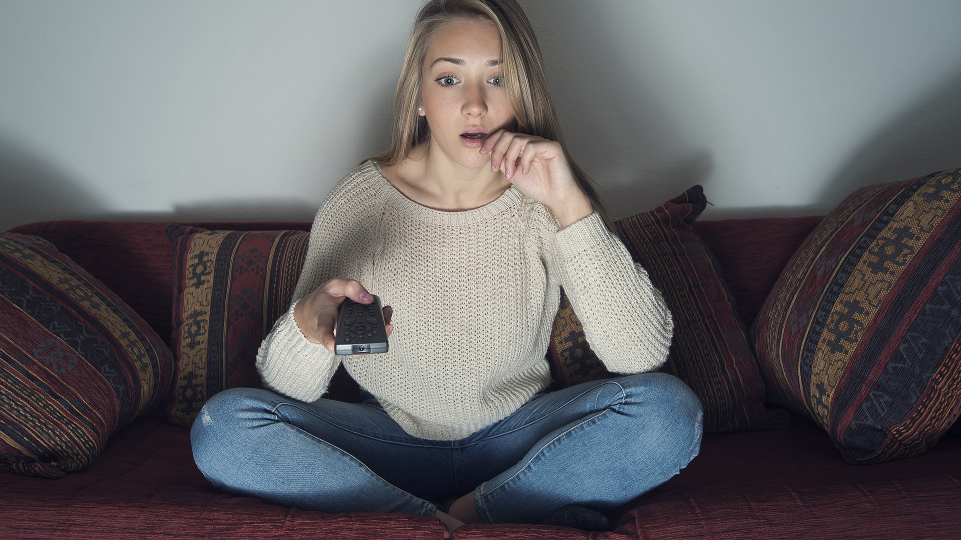 Young woman shocked watching a film and pointing remote at the tv