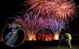 Fireworks over Caerphilly Castle with photographer and tripod in foreground and roundel of remote shutter release