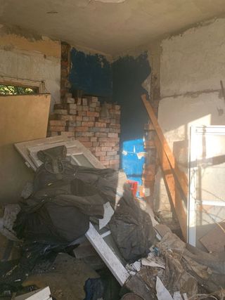 A dilapidated inside wall and bin bags and rubble inside a bungalow