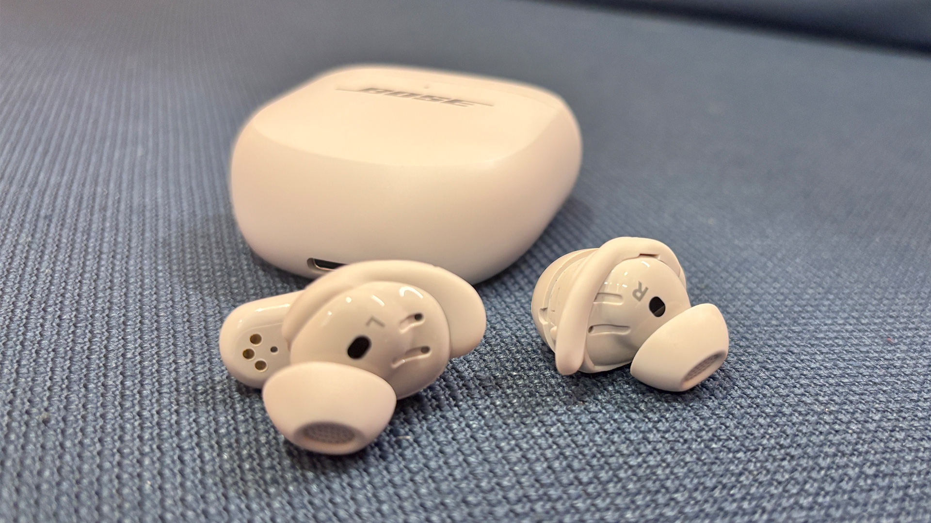 Bose QuietComfort Ultra Earbuds (2nd Gen) wireless earbuds on grey surface in front of charging case