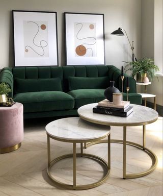 A living room with a dark green couch with two wall art prints above it and two marble nesting tables with books on top