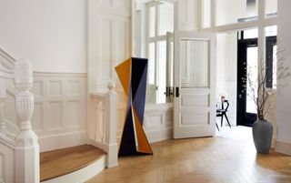 White entryway with half-panelled walls and an orange and blue sculpture