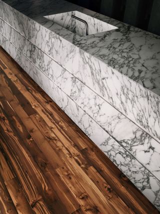 A marble counter alongside dark reclaimed wood kitchen flooring.