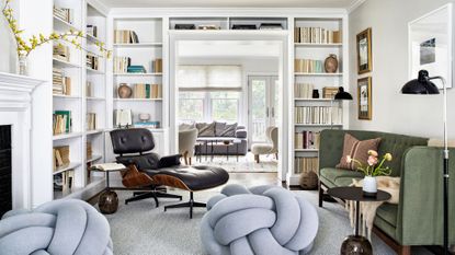 living room with white walls and bookshelves, eames chair and dark green sofa