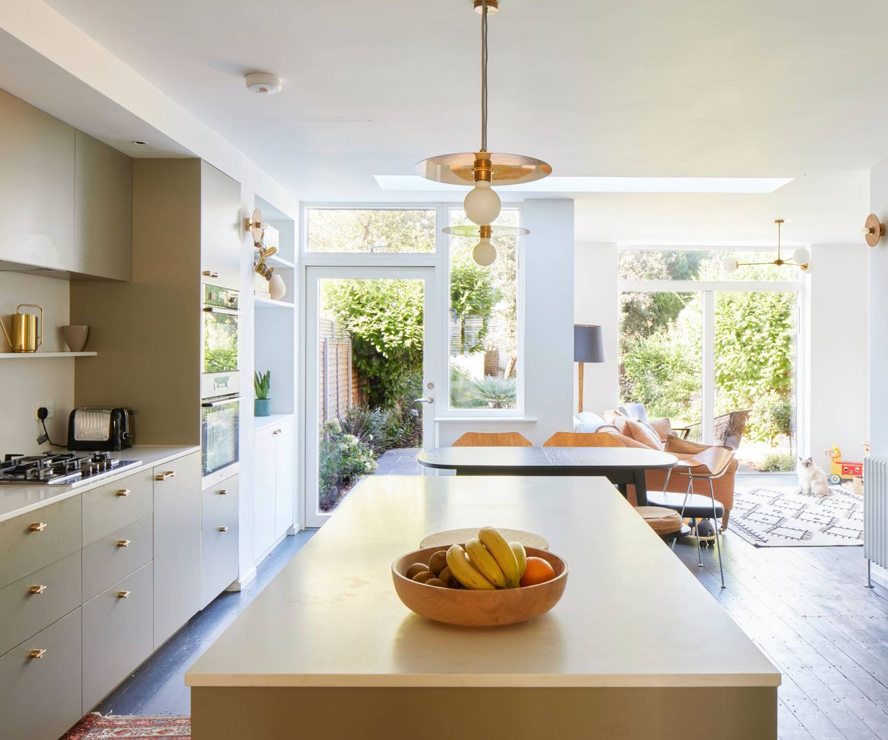 open plan kitchen diner with pale cabinets, large island, dining table and white and glass doors to exterior