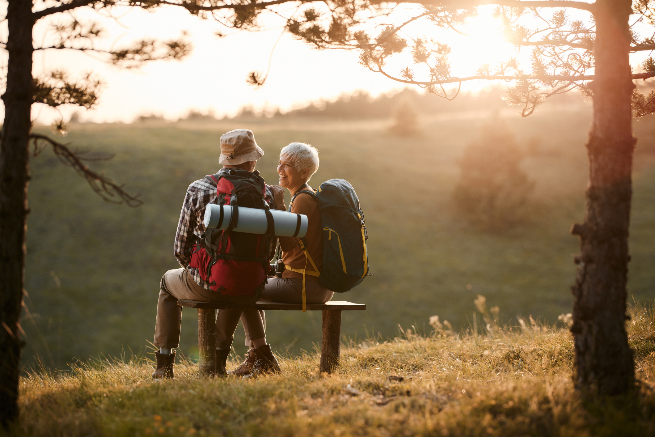 A senior couple with backpacking gear sits on a bench.