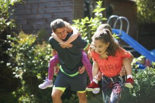 Family playing piggyback races in the garden for a sports day.