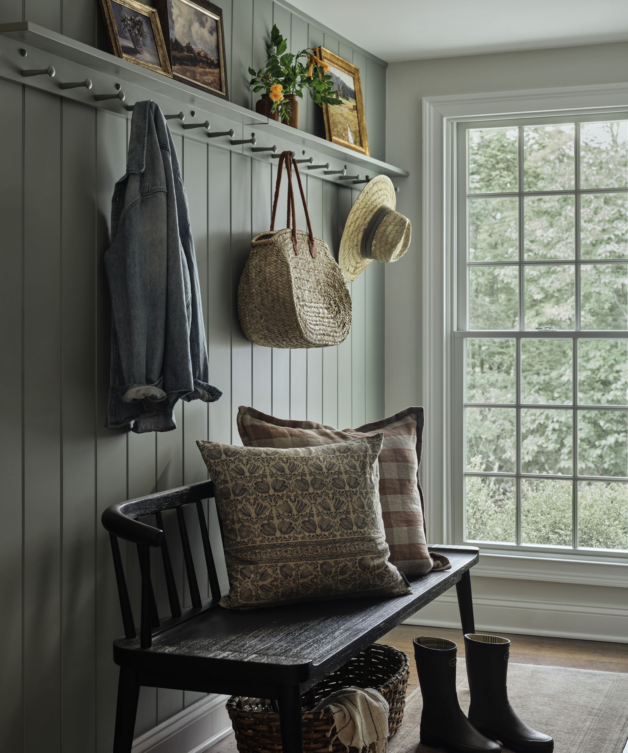 a small blue gray mudroom with panelled walls with pegs for hanging and an antique bench