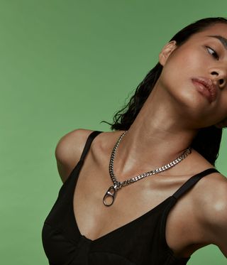 Woman wearing a silver chain necklace against a green background
