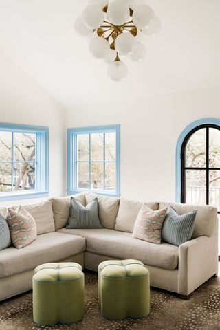 A family room with blue trim, a large linen corner sofa and green foot stools with blue stitching