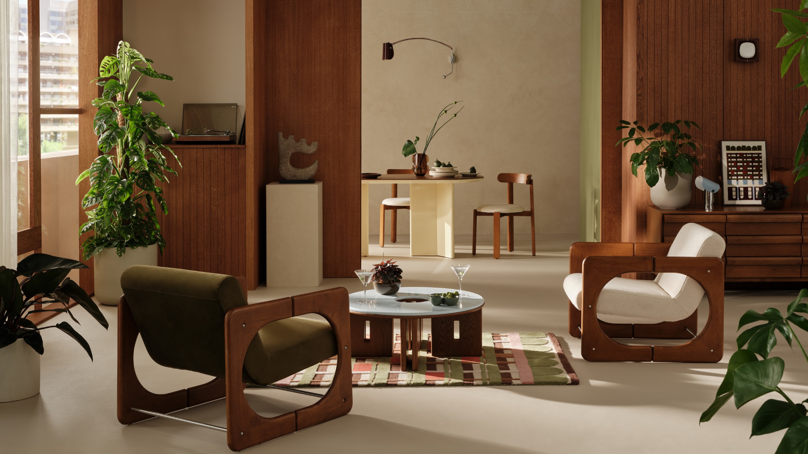 A living room at the Barbican with a view through to the dining room, both furnished with furniture and homewares from the MADE x Barbican collection including retro armchair and a round coffee table