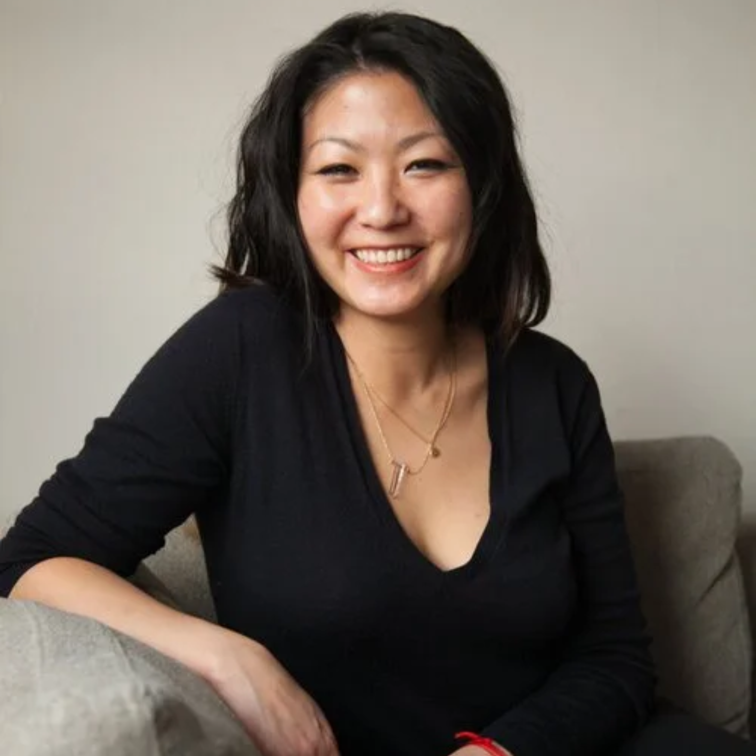 A woman with black hair in a black v-neck long sleeved t-shirt with a pair of necklaces