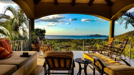 Outside deck in Costa Rica overlooking an ocean with palm fronds and patio chairs