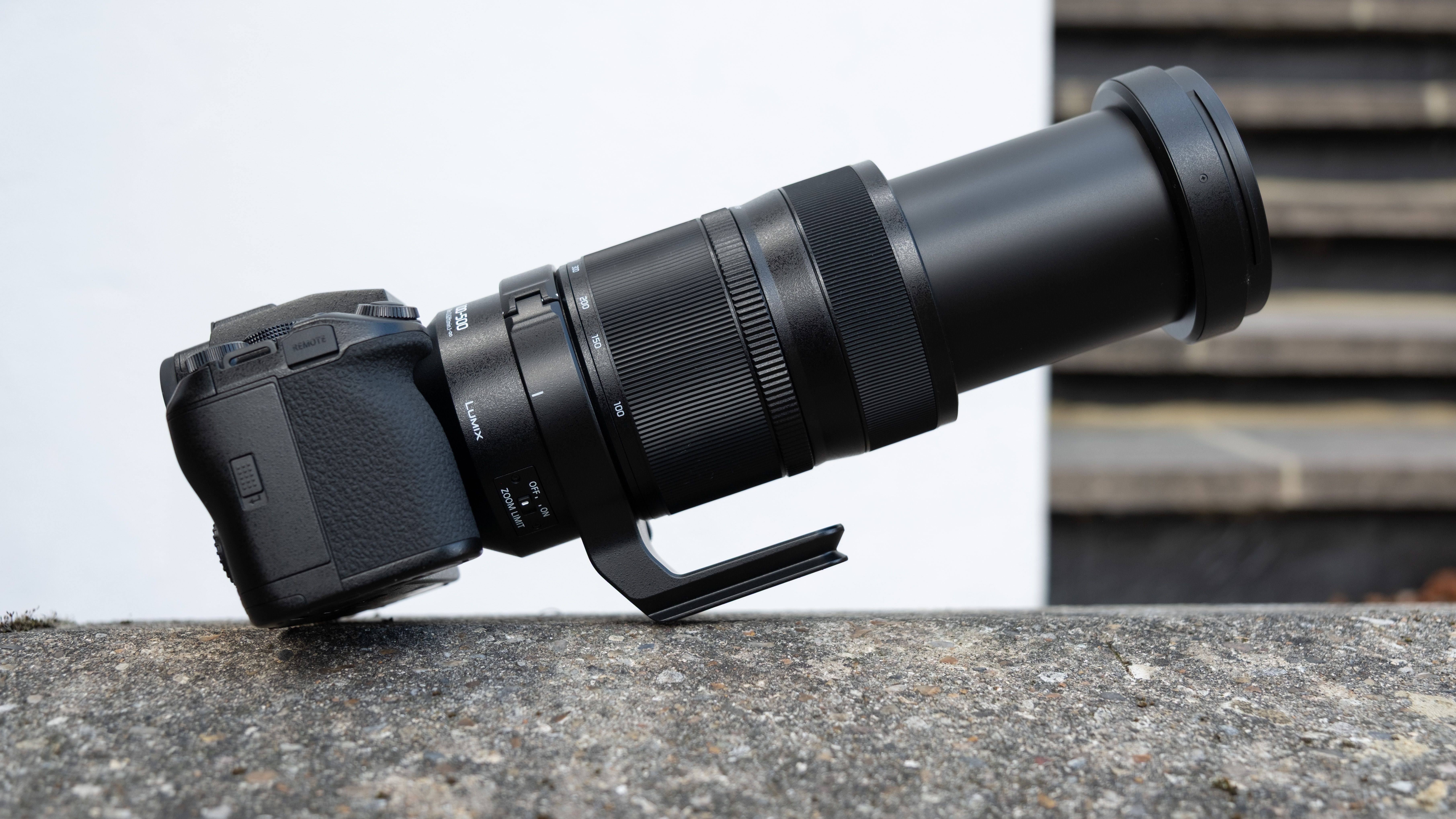 Panasonic Lumix S1II camera with a Lumix S 100-500mm f/5-7.1 lens attached balanced on a wall