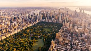 Aerial view of New York City skyline with Central Park and Manhattan, USA. A green-shaped slim rectangle full of trees and lakes is surround by towering skyscrapers against the blue day sky.