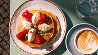 Pancakes with strawberries on top sitting next to coffee