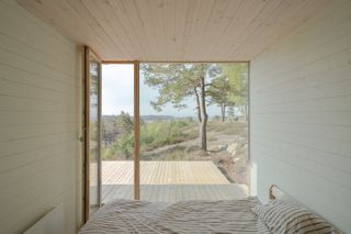 A room with a large window and a bed, with white painted timber walls