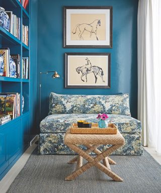 Fitted bookshelves with cupboards below, wooden flooring and rug, blue patterned daybed and drawings of horses on a blue wall.