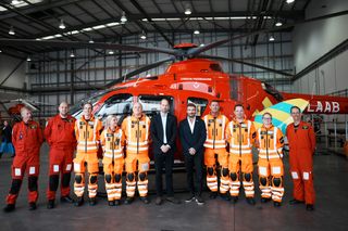 Prince William and David Beckham posing with rescue workers in front of a red helicopter