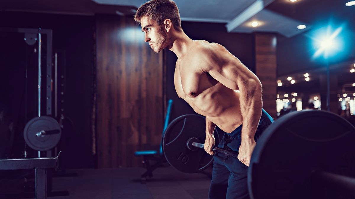 Man performing a barbell bentover row with top off in the gym