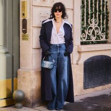 woman wears white button down, pinstripe duster coat, wide-leg jeans, and a mini denim valentino bag
