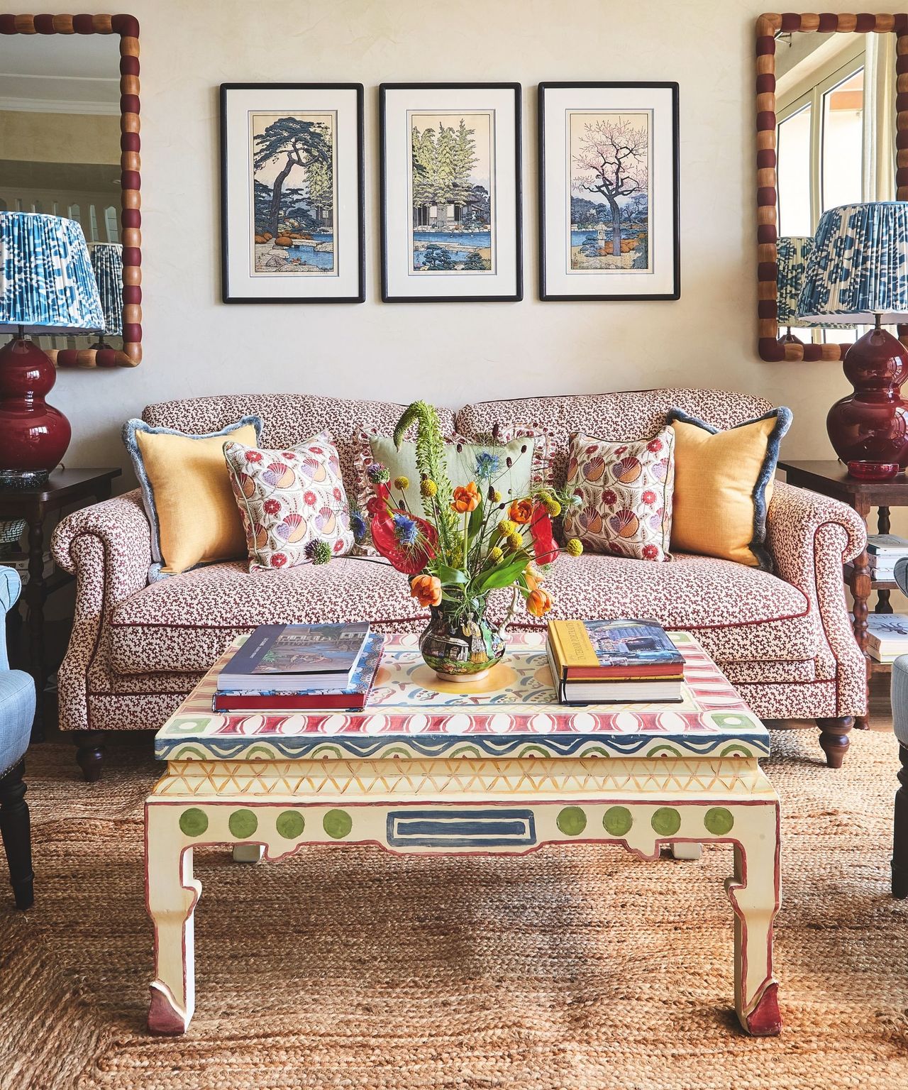 living room with patterned sofa and armchair and textured seagrass rug and colourgul painted wooden coffe table and art on walls behind with symmetrical mirrors