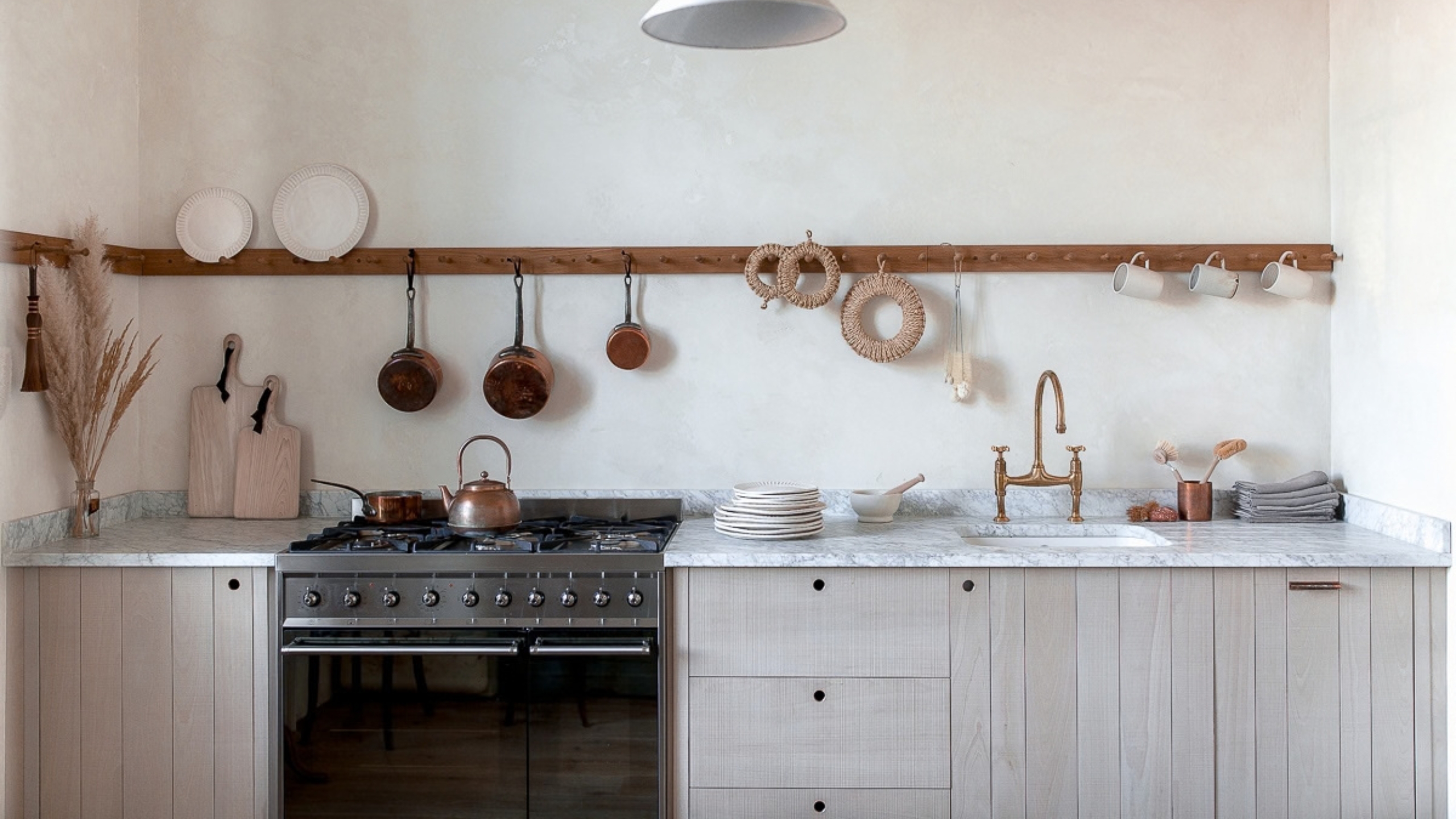 A light wood kitchen with white walls and a medium wood peg rack holding copper kitcheware