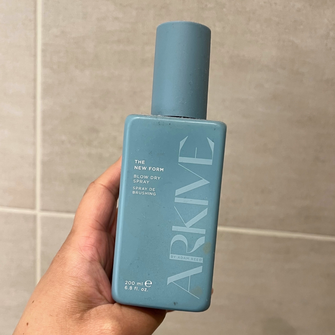 Hand holding blue bottle of ARKIVE Headcare The New Form Blow Dry Spray