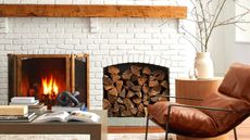 A living room with a white brick walll, a fireplace with logs next to it, a wooden coffee table with books on it, and a brown leather armchair