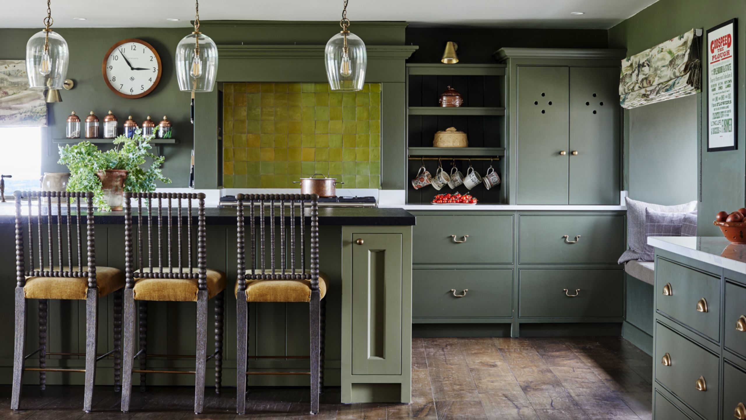 Green kitchen with island, wooden bar stools, yellow backsplash tiling, wooden floor