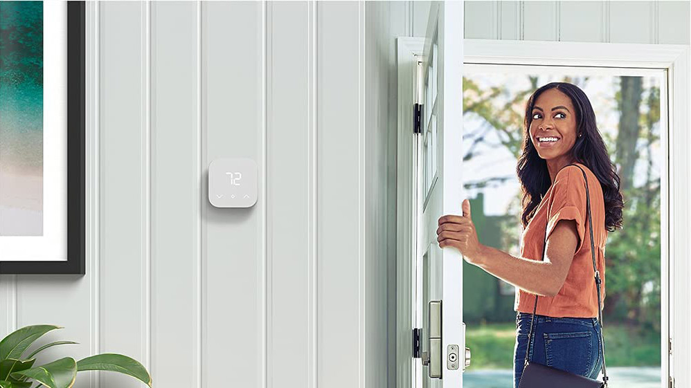 The Amazon Smart Thermostat on a wall next to a door with a woman entering
