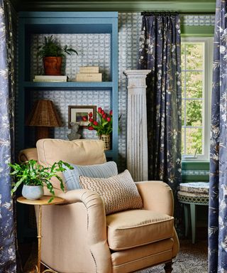 A blue bedroom with patterned wallpaper and drapery, and a beige armchair