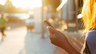 A woman using a smartphone, with sun shining in the distance